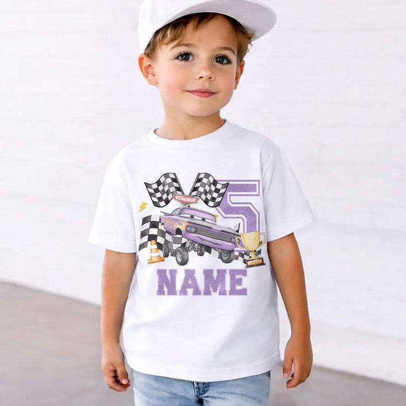 Pode incluir: Camiseta branca com um design de carro de corrida roxo, n&uacute;mero 5, bandeiras quadriculadas e um trof&eacute;u dourado. A palavra "NAME" est&aacute; em letras roxas. A camiseta &eacute; usada por uma crian&ccedil;a, ideal para um anivers&aacute;rio.