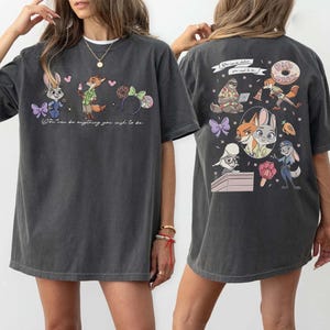 Puede incluir: Camiseta gris oscuro con personajes de dibujos animados de Zootopia. La parte delantera muestra a Judy Hopps, Nick Wilde y unas orejas de Minnie. La parte trasera presenta m&aacute;s personajes de Zootopia y la frase "You can be anything you wish to be."