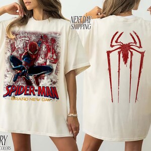 以下が含まれることがあります： アイボリー色のTシャツ。前面にはスパイダーマンのグラフィック、赤と金の「SPIDER-MAN BRAND NEW DAY」の文字。背面には大きな赤いクモのシンボル。快適な色で作られています。