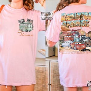 Puede incluir: Camiseta rosa claro con un dise&ntilde;o de furgoneta verde y banderas de cuadros en la parte delantera, con el nombre "Name" impreso debajo. La parte trasera presenta un dise&ntilde;o de "Radiator Springs" con coches de dibujos animados.