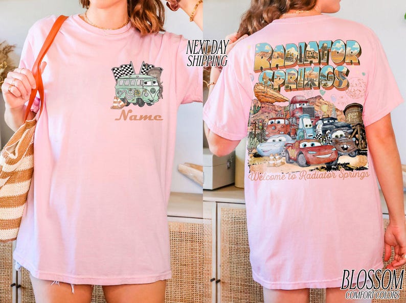 Puede incluir: Camiseta rosa claro con un dise&ntilde;o de furgoneta verde y banderas de cuadros en la parte delantera, con el nombre "Name" impreso debajo. La parte trasera presenta un dise&ntilde;o de "Radiator Springs" con coches de dibujos animados.