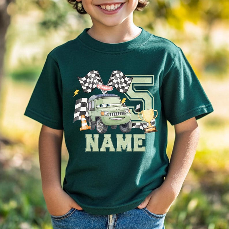 Pode incluir: T-shirt verde escuro com um carro de desenho animado, bandeiras quadriculadas, um trof&eacute;u e o n&uacute;mero 5. A palavra "NAME" &eacute; impressa em letras brancas grandes abaixo do gr&aacute;fico do carro. Um design divertido para o anivers&aacute;rio de uma crian&ccedil;a.