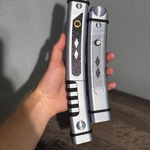 Pu&ograve; includere: Due spade laser argentate con dettagli neri e viola. La spada laser pi&ugrave; grande ha una parte superiore dorata e un'impugnatura nera. La spada laser pi&ugrave; piccola ha una parte superiore argentata e un'impugnatura nera. Entrambe hanno un motivo a diamante.