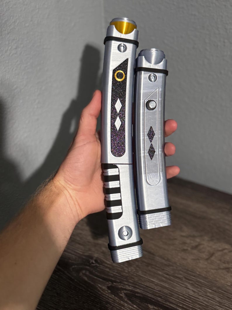 Pu&ograve; includere: Due spade laser argentate con dettagli neri e viola. La spada laser pi&ugrave; grande ha una parte superiore dorata e un'impugnatura nera. La spada laser pi&ugrave; piccola ha una parte superiore argentata e un'impugnatura nera. Entrambe hanno un motivo a diamante.