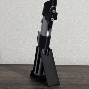 Pu&ograve; includere: Una replica di spada laser argento e nera con un supporto nero. La spada laser ha un'impugnatura cilindrica con dettagli argento e neri e un emettitore nero. Il supporto &egrave; nero e angolato, progettato per l'esposizione.