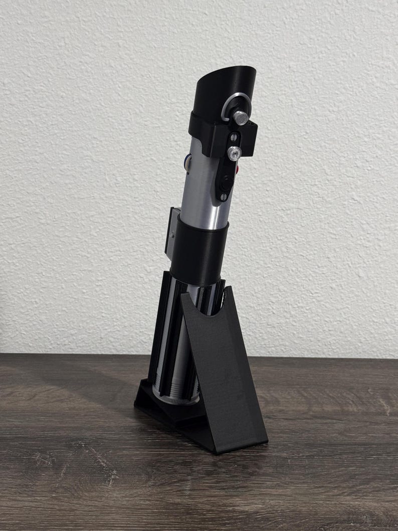 Pu&ograve; includere: Una replica di spada laser argento e nera con un supporto nero. La spada laser ha un'impugnatura cilindrica con dettagli argento e neri e un emettitore nero. Il supporto &egrave; nero e angolato, progettato per l'esposizione.