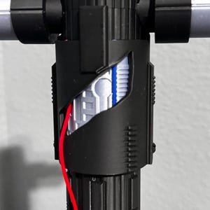 May include: A black lightsaber hilt with silver crossguard arms. The hilt features intricate detailing and a cutaway section showing internal components, including a red wire. This is a prop or toy lightsaber, suitable for cosplay.
