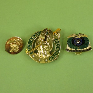 May include: Three gold-colored pins with green and blue accents. The center pin features a winged figure holding a sword and a shield with the text "U.S. ARMY RECRUITER". The pin on the left features a winged eagle with crossed rifles. The pin on the right features a winged eagle with a wreath and the text "SUPPORTING VICTORY".
