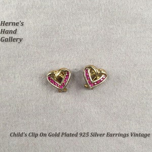 May include: A pair of gold-plated 925 silver clip-on earrings with a heart shape design. The hearts are set with small pink stones.