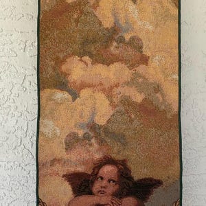 May include: Tapestry table runner featuring a Renaissance-style cherub with a cloud background. The runner has a dark green border and a decorative tassel. The color palette includes shades of brown, gold, and green.