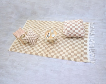 May include: A cozy living space setup featuring a beige and white checkered rug with a matching pillow and small stool. A wooden tray with small white cups and a decorative item sits on the rug, creating a warm and inviting atmosphere.
