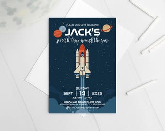 May include: A navy blue invitation card with a space theme. The card features a rocket ship, planets, and stars against a dark blue background. Text includes "Jack's seventh trip around the sun" and event details.
