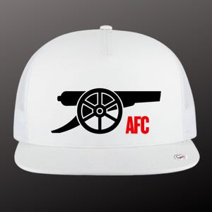 May include: A white baseball cap featuring a black graphic of a cannon centered on the front panel. Below the cannon, the letters AFC are printed in a bold red font. The cap has a structured crown and a flat brim with a small circular sticker.