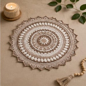 Puede incluir: Un tapete de ganchillo redondo e intrincado con patrones circulares concéntricos en tonos alternos de crema, beige y blanco. El diseño incluye puntos texturizados, un borde festoneado y un motivo floral central con aspecto detallado.