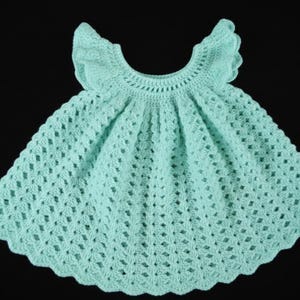 May include: A light turquoise crochet dress with a scalloped hem and ruffled sleeves. The dress features a detailed openwork pattern and is likely handmade. The dress is displayed against a black background.