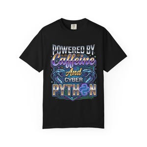 Op de afbeelding: Zwart T-shirt met een kleurrijke afbeelding met de tekst "POWERED BY Caffeine And CYBER PYTHON". Het ontwerp toont een gestileerde slang en een levendig kleurenschema van paars, blauw en goud.