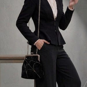 May include: Black peplum blazer and matching trousers. The blazer has a fitted silhouette with a chain strap bag. The bag is black with a silver spiderweb design. The outfit is completed with a white blouse.