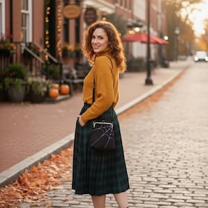 May include: A woman wearing a mustard yellow turtleneck sweater and a green plaid skirt. She is carrying a black purse with a white spiderweb design. She is wearing brown ankle boots and standing on a brick-paved street.