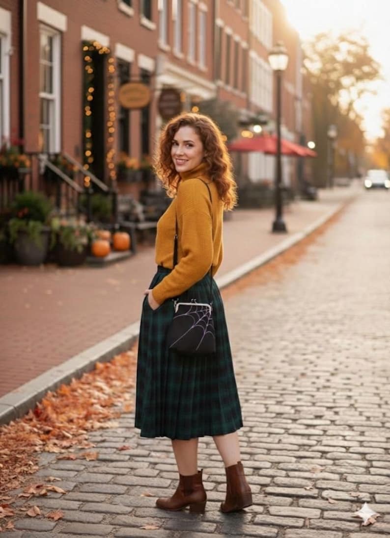 May include: A woman wearing a mustard yellow turtleneck sweater and a green plaid skirt. She is carrying a black purse with a white spiderweb design. She is wearing brown ankle boots and standing on a brick-paved street.