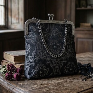 May include: A black handbag featuring a dark gray damask pattern, a silver-toned metal frame with a kiss-lock clasp, and a silver chain strap. The bag has a structured rectangular shape with rounded corners and a textured fabric exterior.