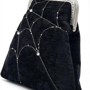 May include: Black velvet clutch with a silver clasp. The clutch features a decorative pattern of silver stitching and sparkling embellishments. A stylish accessory for special occasions.