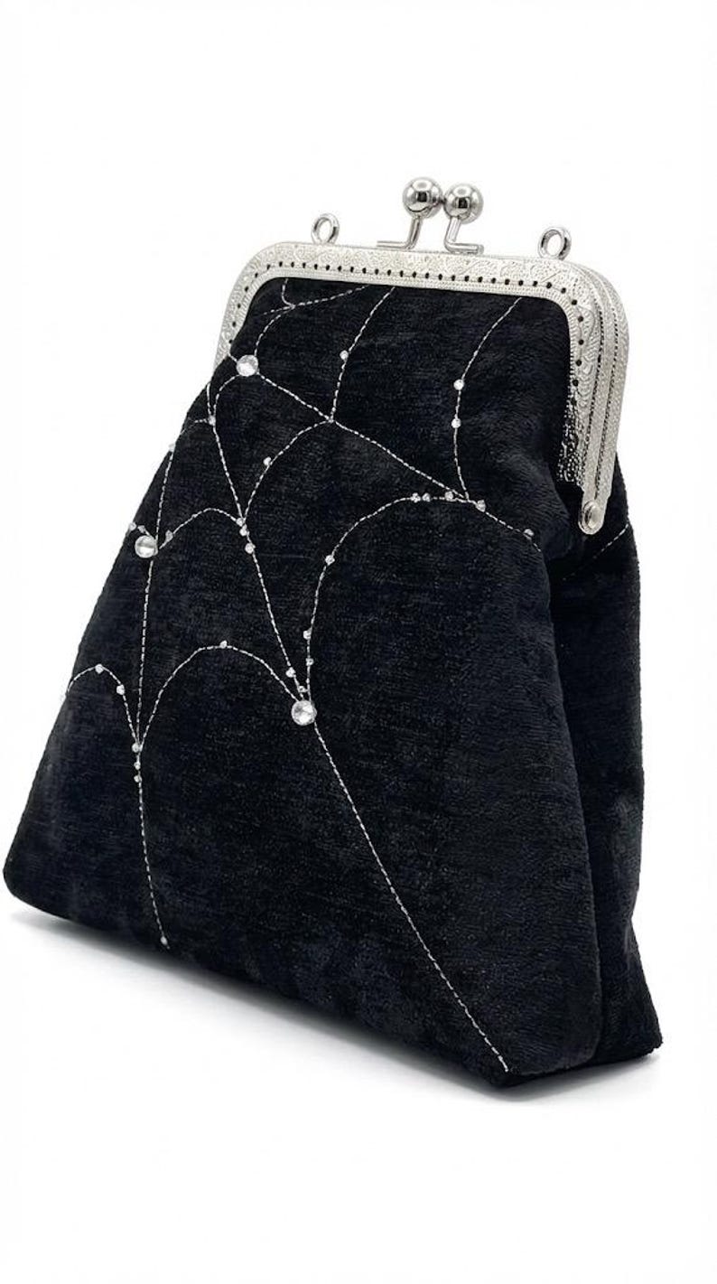 May include: Black velvet clutch with a silver clasp. The clutch features a decorative pattern of silver stitching and sparkling embellishments. A stylish accessory for special occasions.