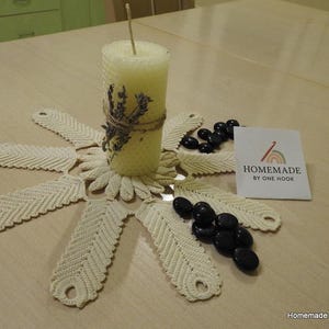 May include: A handmade beeswax candle with dried lavender and a decorative crochet doily. The candle is surrounded by black stones and a card that reads "Homemade by One Hook". The doily has a unique feather design.