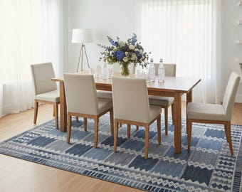 Könnte beinhalten: Ein Esszimmer-Set mit einem rechteckigen Holztisch und sechs beige gepolsterten Stühlen. Unter dem Tisch liegt ein blau-weiß gemusterter Teppich. Auf dem Tisch steht eine Vase mit blau-weißen Blumen, Gläsern und Wasserflaschen. Der Tisch ist ca. 180 cm lang.