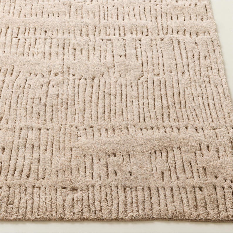 Puede incluir: Una alfombra rectangular beige con un patr&oacute;n texturizado en relieve. El dise&ntilde;o presenta l&iacute;neas verticales y horizontales, creando una apariencia tejida. La alfombra est&aacute; hecha de un material suave, adecuado para una sala de estar o un dormitorio.
