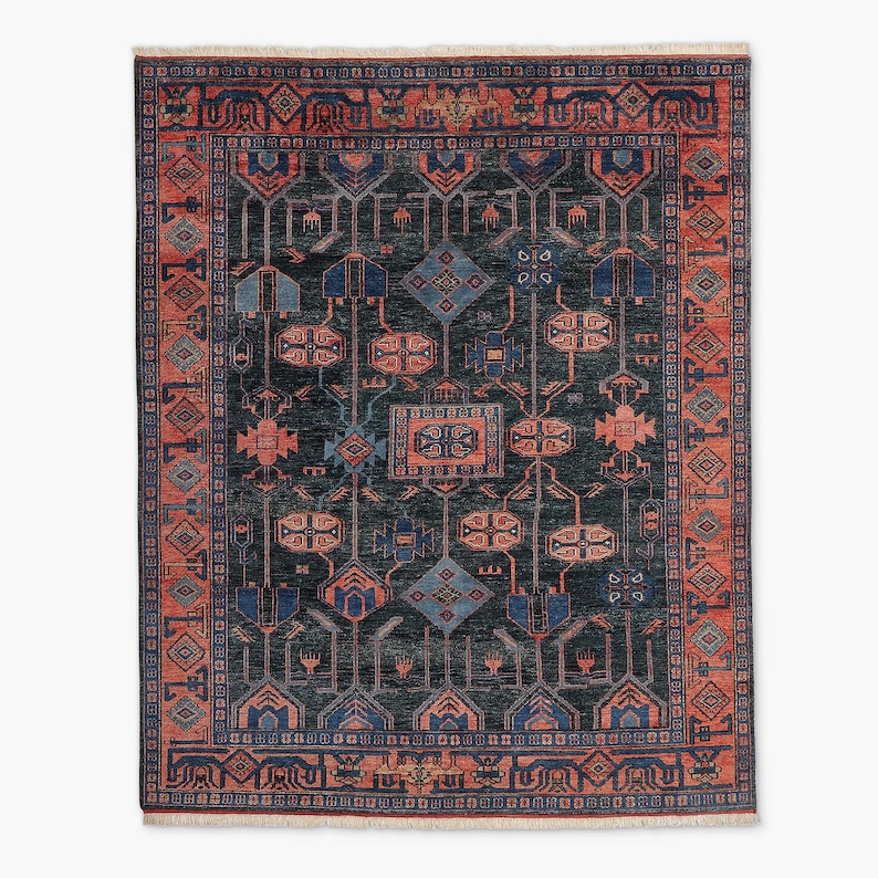 K&ouml;nnte beinhalten: Ein rechteckiger Teppich mit dunkelblaugr&uuml;nem Hintergrund und einem detaillierten geometrischen Muster in Blau- und Korallt&ouml;nen. Der Teppich hat einen Rand mit sich wiederholendem Design und Fransen.