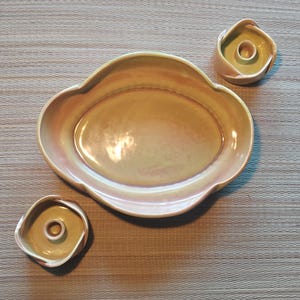 May include: A set of three ceramic pieces in a warm, iridescent color palette. The set includes an oval-shaped serving dish and two small, square-shaped candle holders. The pieces have a glossy finish and a unique, organic design.