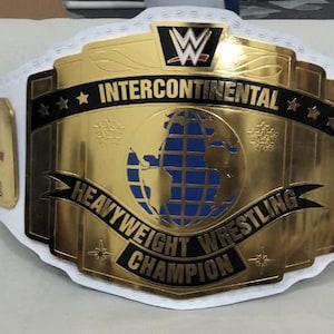 May include: A gold and white Intercontinental Heavyweight Wrestling Champion belt. The belt features a gold center plate with a blue and gold globe design, the words "Intercontinental" and "Heavyweight Wrestling Champion". The belt has a white strap.