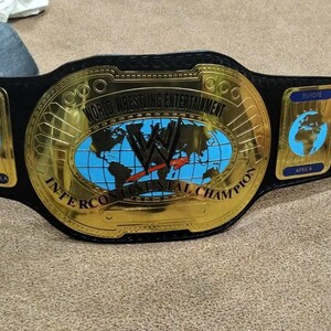 May include: A gold and black Intercontinental Championship belt. The center plate features a world map and the text "World Wrestling Entertainment". Side plates display continents. The belt is made of leather and metal.