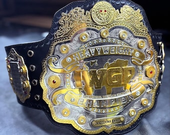 May include: A professional wrestling championship belt with a black leather strap and a large, ornate silver and gold buckle. The buckle features the text "Heavyweight" and "IWGP Champion". Red gemstones are set into the design.