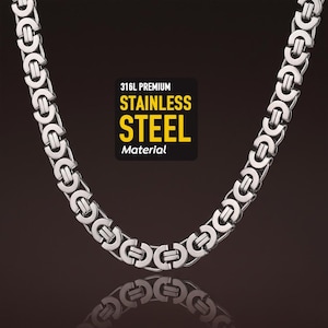 May include: A silver-colored stainless steel chain necklace with a distinctive interlocking design. The image includes a black and yellow label that reads "316L Premium Stainless Steel Material". The necklace is displayed against a dark background.