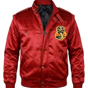 May include: A red satin bomber jacket with a black lining and a Cobra Kai patch on the chest. The jacket features a zipper closure, snap buttons, and a ribbed collar and cuffs. The jacket has a classic bomber style with a modern twist.