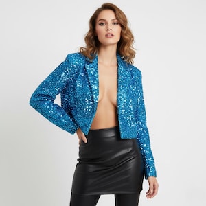 May include: A cropped, open-front blazer in a vibrant turquoise hue, fully embellished with sequins. The jacket features long sleeves and a classic notched lapel. Paired with a black leather mini-skirt and black leggings.