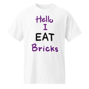 Op de afbeelding: Wit T-shirt met de tekst "Hello I EAT Bricks" in paars en zwart. Het T-shirt heeft een ronde hals en korte mouwen. De tekst is gecentreerd, waardoor het een casual kledingstuk is.