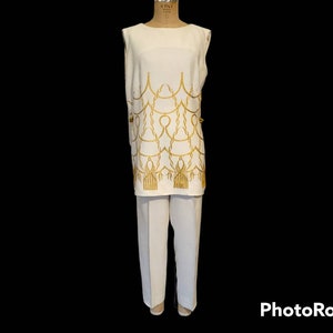 May include: A white sleeveless top with a gold chain pattern and matching white pants. The top has a scoop neck and the pants have a straight leg.