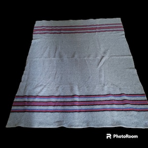 May include: A gray wool blanket with red, blue, and black stripes. The blanket is folded in half and has a textured surface.
