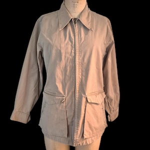 May include: A tan zip-up jacket with a collared neckline and two front pockets. The jacket is displayed on a mannequin. The sleeves are long and the jacket is made of a lightweight material.