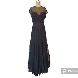 May include: A black lace gown with a sheer bodice and a tiered skirt. The gown has a fitted bodice and a flowing skirt.