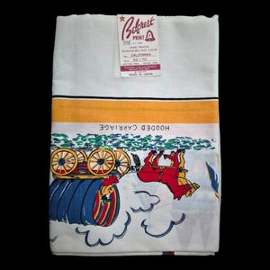 May include: A white rectangular tablecloth featuring a Belcrest Print label and a graphic illustration of a horse-drawn hooded carriage. The print includes a yellow horizontal stripe, blue wheels, and a red horse with the text HOODED CARRIAGE.