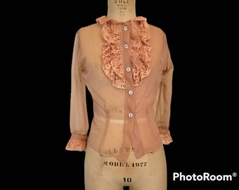 May include: A sheer peach blouse with a lace ruffle collar and button front. The blouse has long sleeves and a fitted waist.
