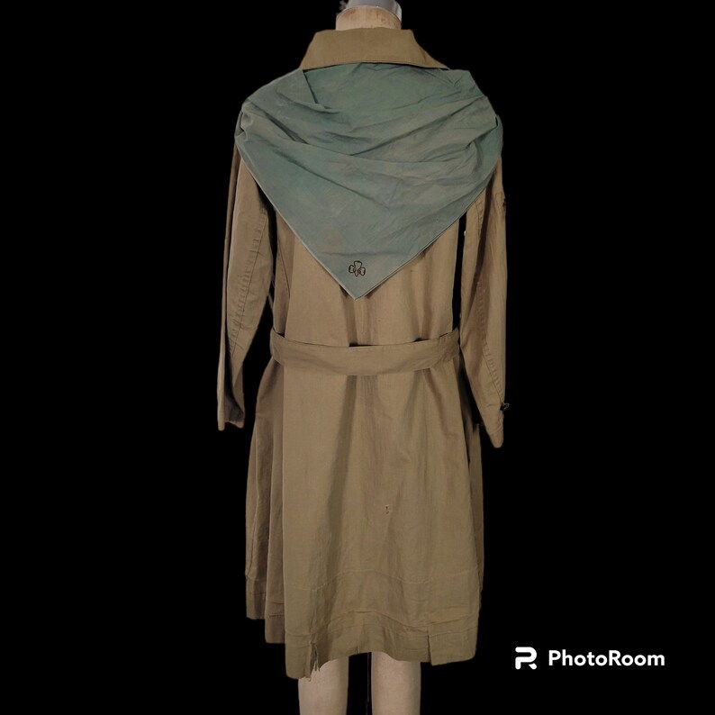 May include: A tan trench coat with a large, light blue scarf attached to the collar. The scarf has a small, embroidered clover design.