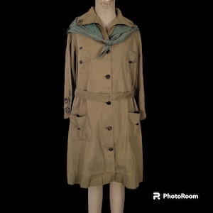 May include: A vintage Girl Scout uniform dress in a khaki color with a green sash and embroidered patches. The dress has a long sleeve, a button-up front, and a belt.