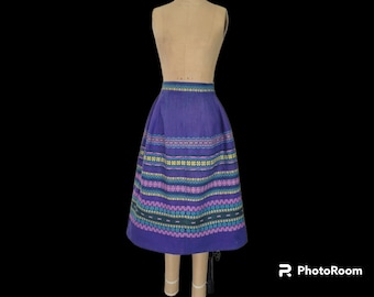 May include: A purple skirt with a colorful embroidered pattern. The skirt has a full, gathered shape and a waistband.