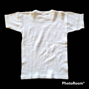 May include: A plain white t-shirt, viewed from the back, with short sleeves and a crew neck. The shirt is made of a soft, likely cotton, material. The garment is displayed against a black background.