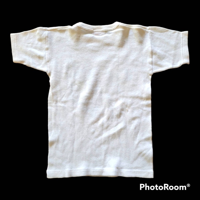 May include: A plain white t-shirt, viewed from the back, with short sleeves and a crew neck. The shirt is made of a soft, likely cotton, material. The garment is displayed against a black background.
