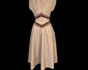 May include: A vintage beige dress with a wrap-style bodice and cap sleeves. The dress features a chevron design in shades of brown at the waist. The skirt is pleated and falls to a midi length, showcasing a classic silhouette.